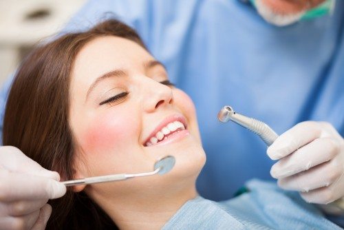 Smiling-Young-Woman-in-Dentists-chair-dentists-gloved-hand-holding-dental-tool.-e1461903556112.jpg